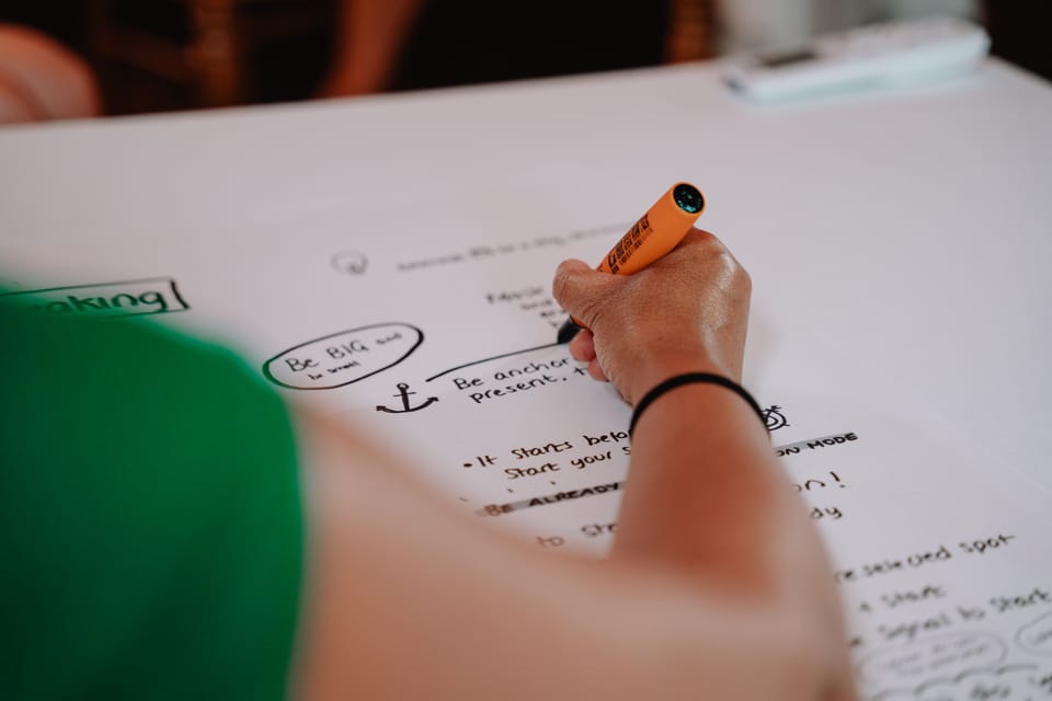 Angel is writing with a felt marker on a big sheet of paper to cover what is being spoken about